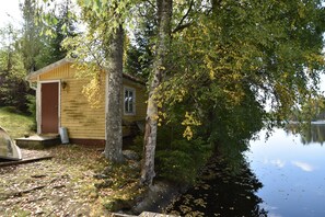 Une petite cabane en bois au bord d’un lac, entourée d’arbres et d’un quai.