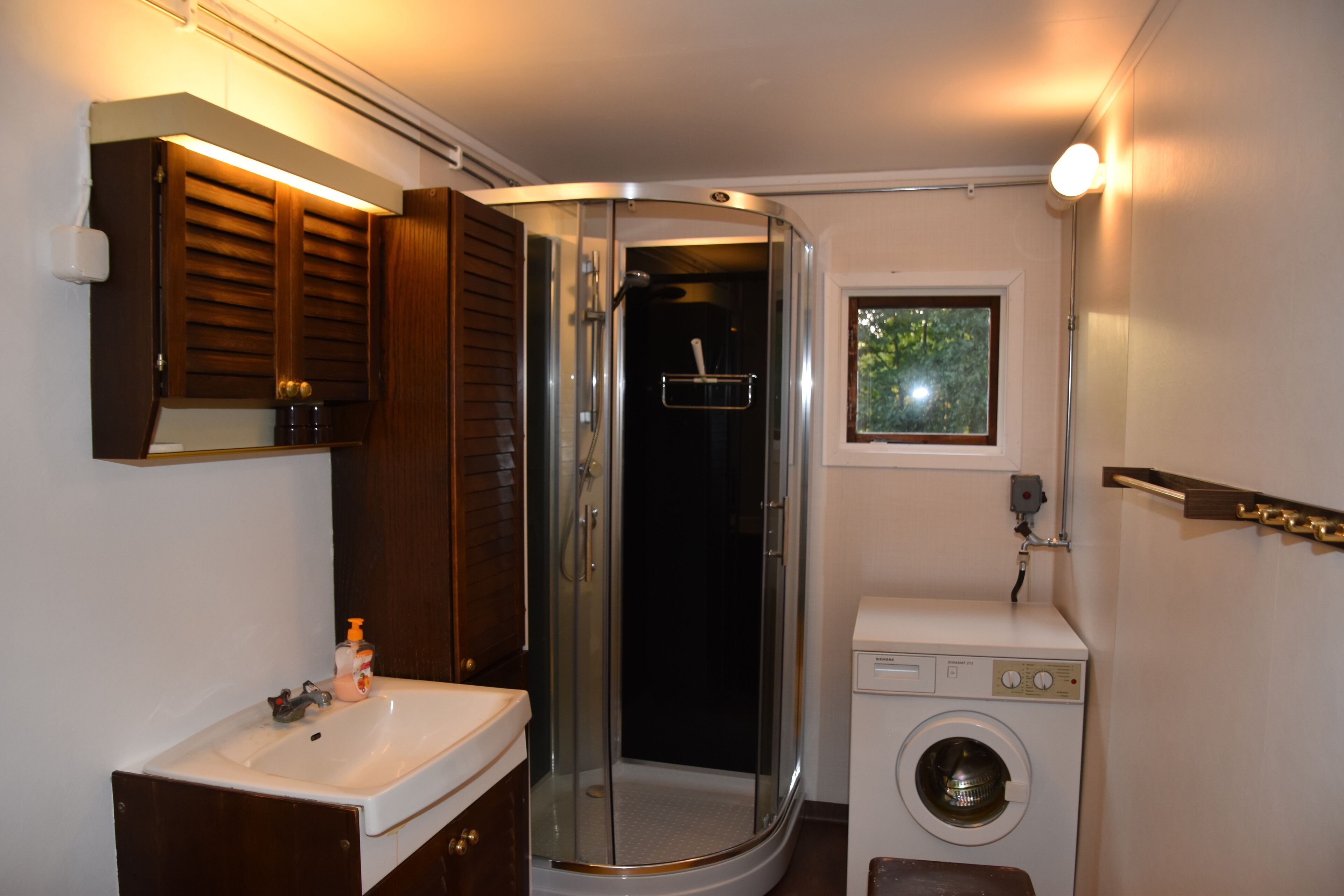 A compact bathroom with a glass-enclosed shower, a sink, and a washing machine.