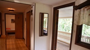 Un pasillo con suelo de madera que lleva a una habitación con cama y ventana con vistas a un balcón.