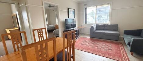 A living room with a dining table, chairs, a sofa, a TV, and a window.