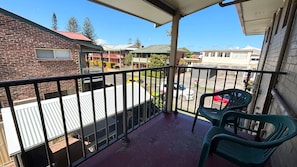 A balcony with a metal railing, a green plastic chair, and a view of a street with buildings and parked cars.