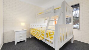 Ein Etagenbett mit einer Leiter, ein Nachttisch mit Lampe und ein Fenster mit Blick auf Bäume.