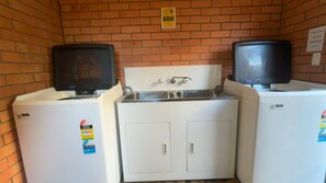 A laundry room with two washing machines and two dryers, a sink, and a brick wall. - Cameo Court 1 - walk to the beach (SOUTH WEST ROCKS)