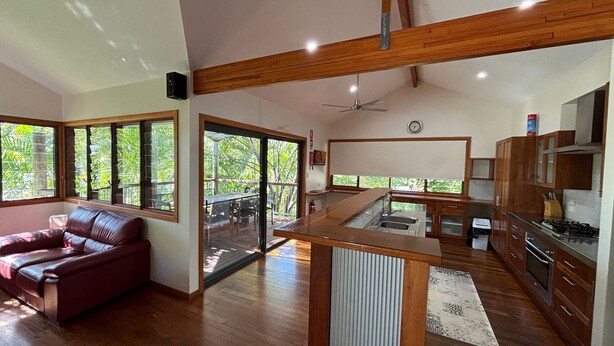 A spacious living area with a large window, a wooden ceiling, and a kitchen with wooden cabinets. - Amaroo - walk to the bay - Bring your own linen (ARAKOON)