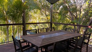 A wooden deck with a table and chairs, surrounded by lush tropical foliage. - Amaroo - walk to the bay - Bring your own linen (ARAKOON)