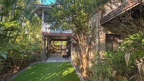 A covered outdoor area with a pathway leading to a building, surrounded by lush greenery. - Amaroo - walk to the bay - Bring your own linen (ARAKOON)