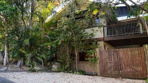 A two-story building with a balcony, surrounded by dense foliage and a gravel driveway. - Amaroo - walk to the bay - Bring your own linen (ARAKOON)