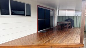 A wooden deck with a sliding glass door, a small table, and a covered grill. - Three/Fifty Four Straight St Hat Head - Bring your own linen (Hat Head)