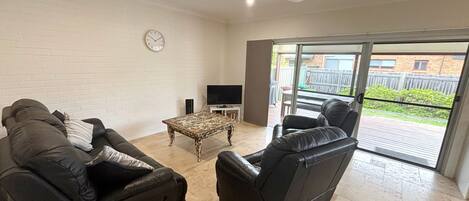 A living room with a sofa, a chair, a coffee table, a TV, and a clock on the wall.