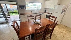 A kitchen with a dining table, chairs, a microwave, oven, and a refrigerator.