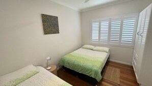 A bedroom with a bed, a bedside table, a lamp, a window with blinds, and a door. - Three/Fifty Four Straight St Hat Head - Bring your own linen (Hat Head)