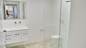 Un baño moderno con lavamanos, espejo e inodoro blancos.