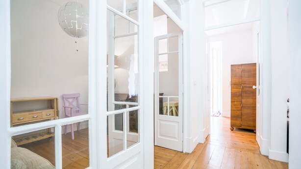 A bright hallway with wooden flooring, white walls, and a wooden door. - Estrela Neoclassical Apt River View (Lisbon)