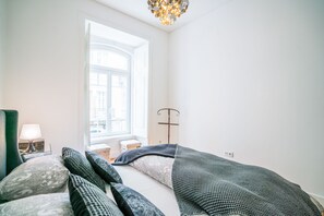 Un dormitorio con un ventanal grande, una cama con ropa de cama estampada, una mesita de noche con una lámpara y una lámpara de pie.