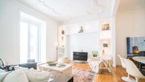 A modern living room with a sofa, coffee table, and a fireplace. There are shelves with decorative items and a painting on the wall. - Estrela Neoclassical Apt River View (Lisbon)