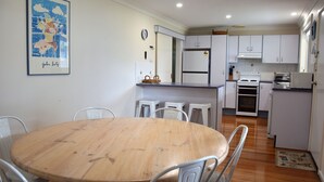 Een compacte keuken met een centraal eiland, witte kasten, en een eethoek met een houten tafel en metalen stoelen.