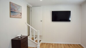 Een kamer met een trap, een flatscreen televisie aan de muur en een schilderij.