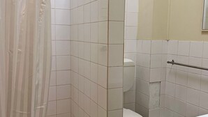 Een badkamer met witte tegels, een douchegordijn en een toilet met een handgreep.