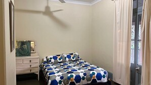 Een slaapkamer met een bed, een kaptafel, een schilderij en een raam met gordijnen.