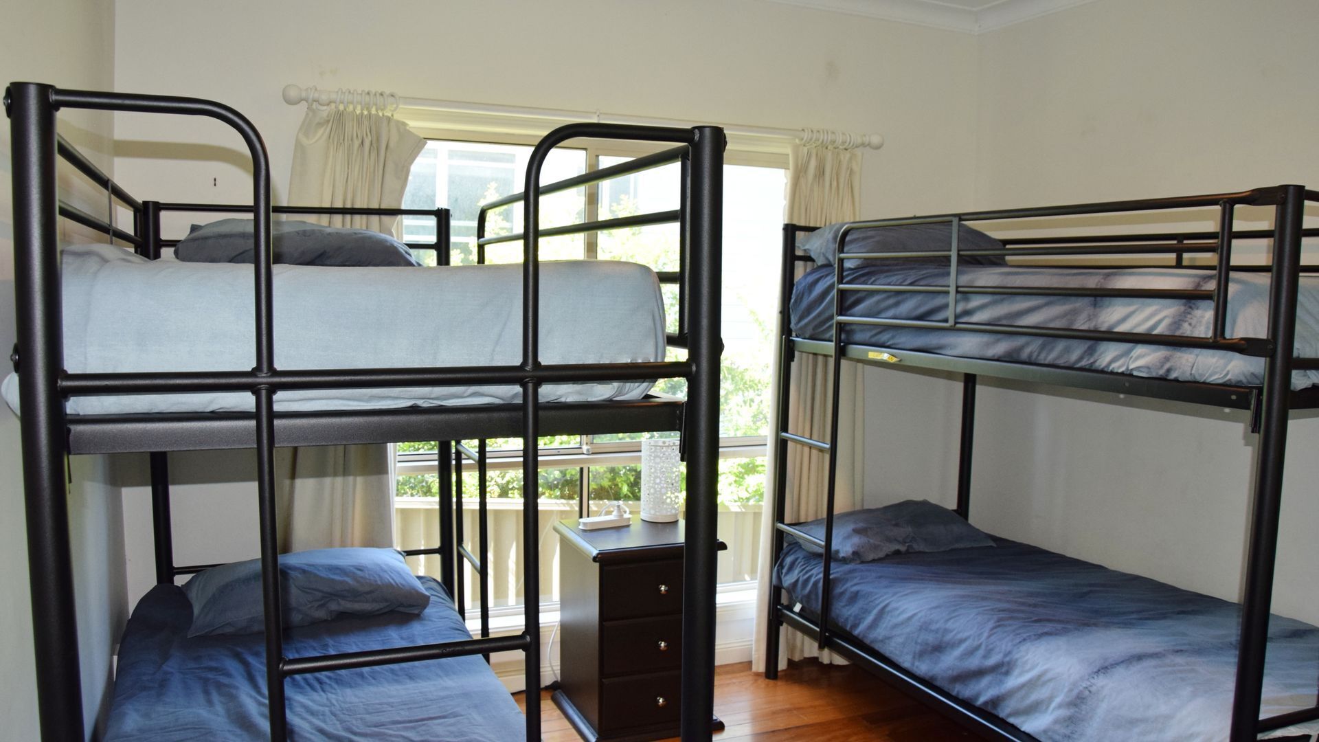 Quarto em dormitório com três beliches, uma cômoda pequena e uma janela com cortinas.