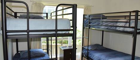 Quarto em dormitório com três beliches, uma cômoda pequena e uma janela com cortinas.