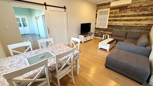 Un soggiorno con un divano, una TV, un tavolo da pranzo con sedie e un pavimento in legno.