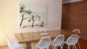 A conference room with a wooden table, white chairs, and a beach-themed painting on the wall.