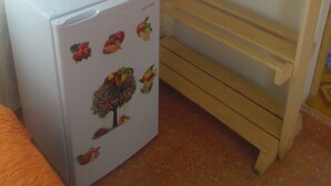 A compact room with a white refrigerator adorned with fruit and vegetable stickers, a small white table with two cups, and a wooden bunk bed with patterned bedding. - Casa Yaquelin y Osmani (Viñales)