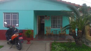 A two-story building with a red roof and teal walls. There is a motorcycle parked in front, and a small garden with a palm tree. - Casa Yaquelin y Osmani (Viñales)