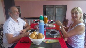 A dining table with a red tablecloth, a glass coffee table, and a bowl of bread rolls. - Casa Yaquelin y Osmani (Viñales)