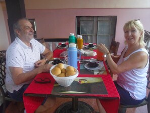Uma mesa de jantar com toalha vermelha, uma mesa de centro de vidro e uma travessa de pães.