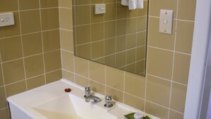 A bathroom with a white sink, two faucets, a mirror, and beige tiled walls. - Wards Holiday Flat 8 (SOUTH WEST ROCKS)