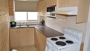 A compact kitchen with beige cabinets, a white stove, a microwave, and a window above the sink. - Wards Holiday Flat 8 (SOUTH WEST ROCKS)