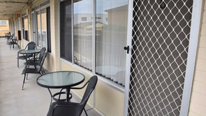 A covered outdoor area with tables and chairs, a glass door with a security screen, and a view of buildings in the background. - Wards Holiday Flat 8 (SOUTH WEST ROCKS)