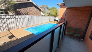 A rooftop pool with a clear blue water surface, surrounded by a wooden deck and a metal railing.