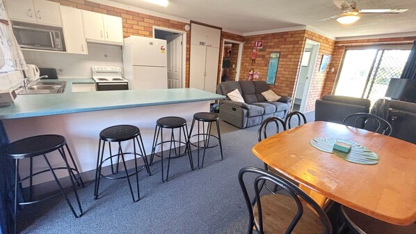 A compact kitchen with a microwave, stove, and refrigerator. There is a bar area with stools and a dining table with chairs.