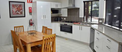 Una cucina moderna con mobili bianchi, fornello, forno e zona pranzo con tavolo e sedie in legno.