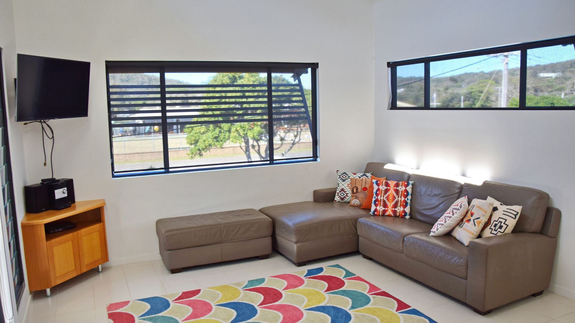 A living room with a sectional sofa, a television, and a window with a view of trees and a fence.
