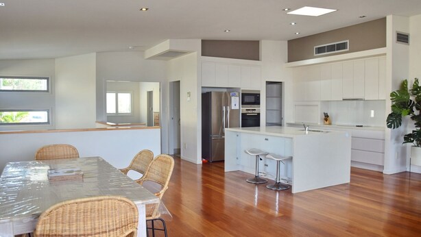 A modern kitchen with white cabinets, stainless steel appliances, and a central island with bar stools. - Cool & Calm - walk to the beach (SOUTH WEST ROCKS)
