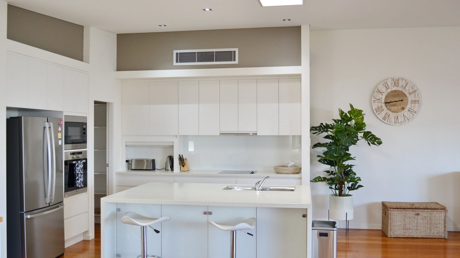 A modern kitchen with white cabinets, stainless steel appliances, a central island with bar stools, a sink, and a decorative clock on the wall.