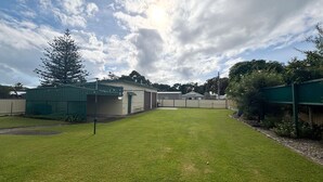 A fenced backyard with a grassy lawn, a tall tree, and a building with a garage. - Mountain View Hat Head - Bring your own linen (HAT HEAD)