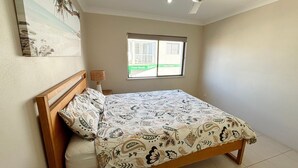 A bedroom with a bed, a window, and a wall-mounted artwork. - Paragon Apartment 3 - walk to the beach (South West Rocks)
