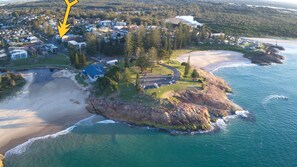 An aerial view of a coastal property with a beach, a small island with a house, and a lighthouse in the distance.