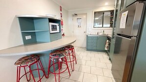 Une cuisine dotée d’un comptoir incurvé, d’un four à micro-ondes, d’un réfrigérateur et de trois tabourets aux assises à motifs.