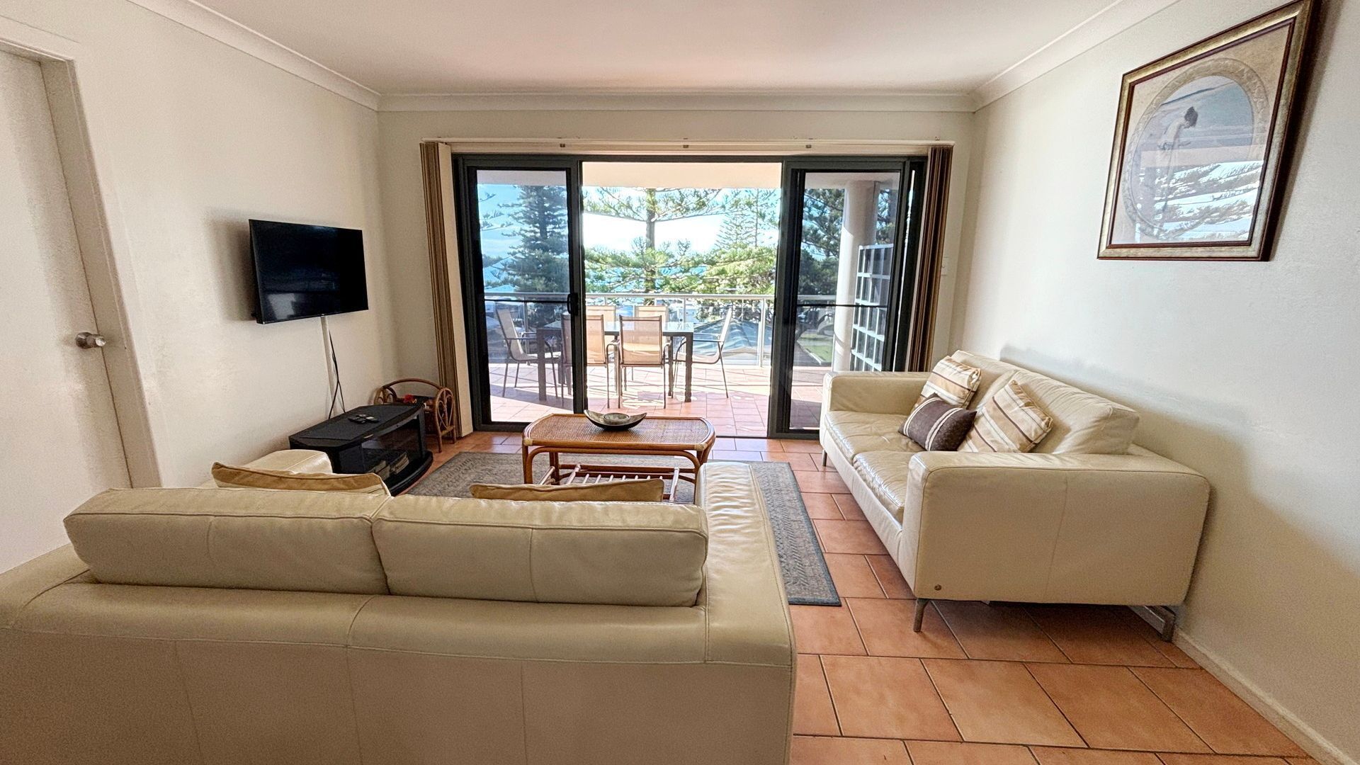 A living room with a sofa, a television, a coffee table, and a view through a glass door to an outdoor patio.