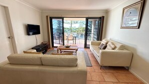 A living room with a sofa, a television, a coffee table, and a view through a glass door to an outdoor patio.