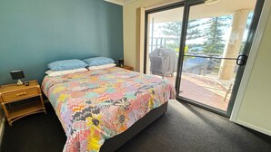 Une chambre à coucher comprenant un lit, une table de chevet, une fenêtre donnant sur l’extérieur et une porte-fenêtre coulissante.