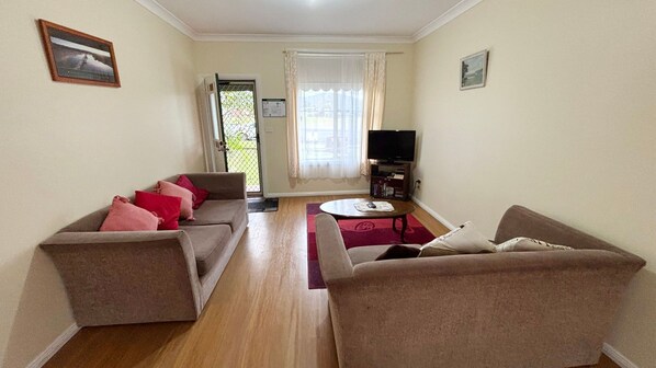 A living room with two sofas, a coffee table, a TV, and a door leading outside. - Chalker's Unit - Bring your own linen (SOUTH WEST ROCKS)