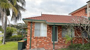 A residential building with a red-tiled roof, brick walls, and a green front porch.