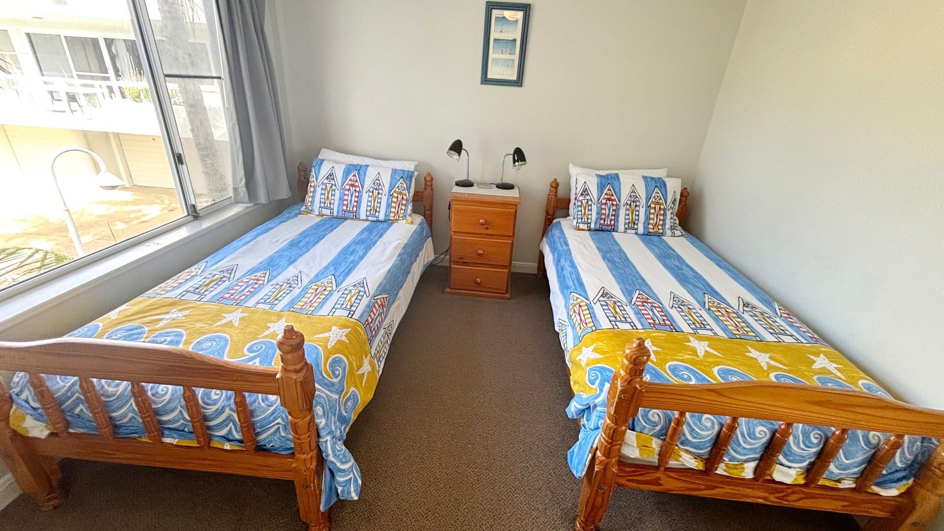 A room with two wooden beds, a nightstand, a lamp, and a window with curtains.